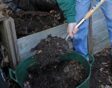 Persoon schept compost uit een compostbak in een grote teil.