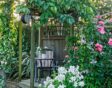 Een knusse achtertuin waar rozen, clematis en klimop zorgen voor een gelaagde, samenhangende look rondom een tuinhuis.