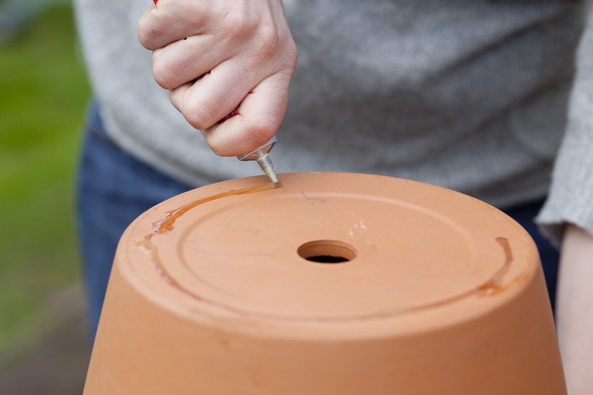 Iemand lijmt de onderkant van een terracotta pot.