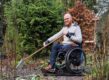 Ralph met een hark in zijn tuin met zijn rolstoel op een rubber mat.