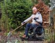 Ralph met een hark in zijn tuin met zijn rolstoel op een rubber mat.