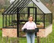 Petra D'hoey voor haar serre met een krat voor planten in haar handen.