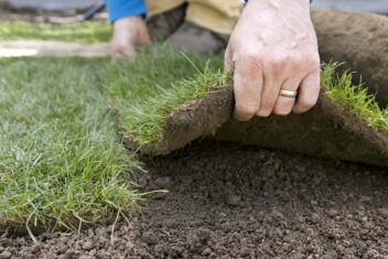 Iemand legt met de hand graszoden op de tuinaarde.