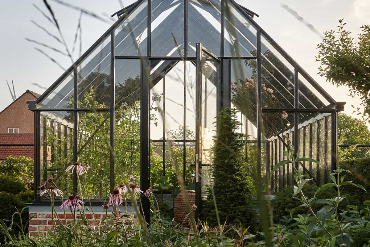 Een serre bij zonsondergang met planten ervoor en een stenen basis.