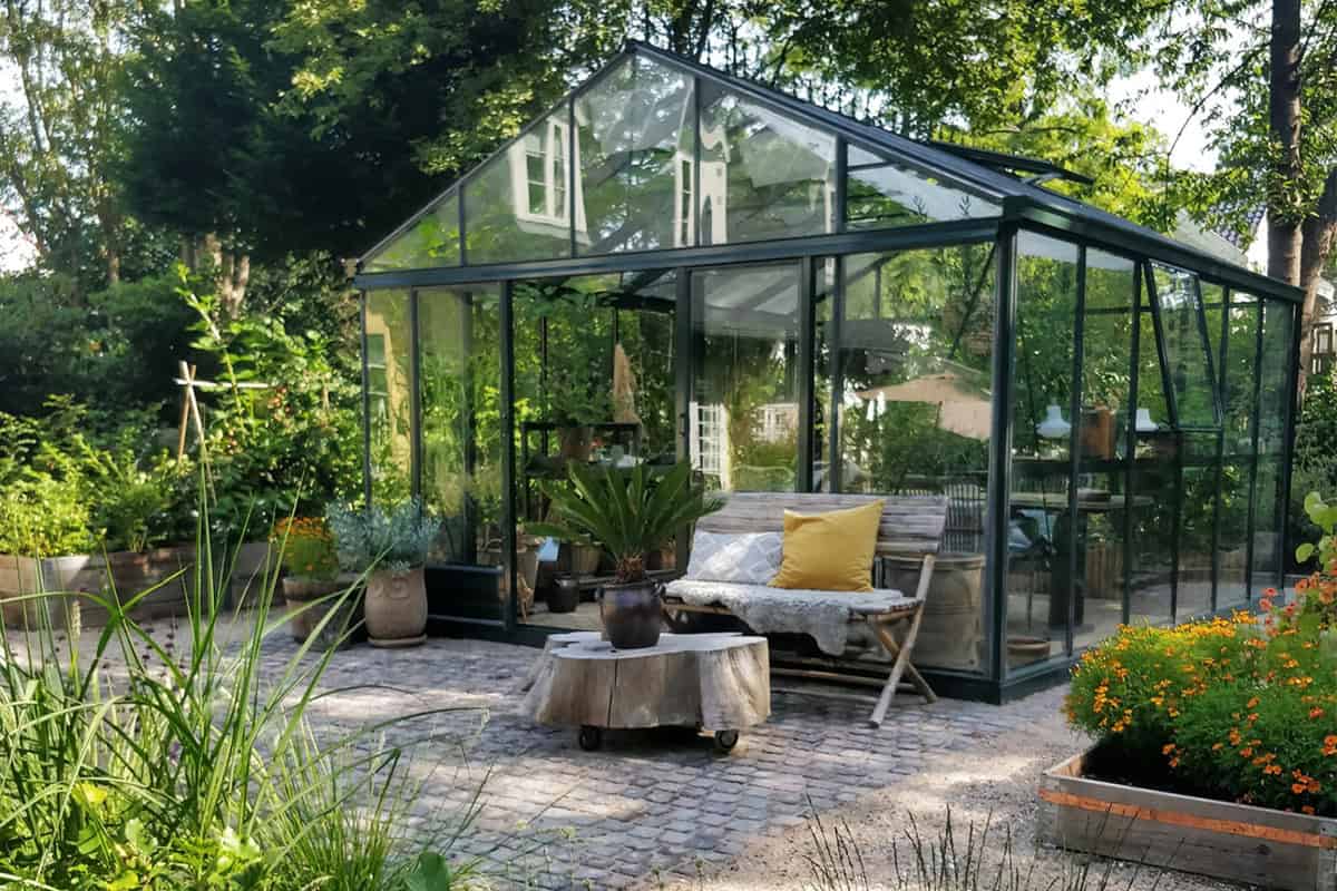 Een serre met een terras ervoor, een bank en planten.