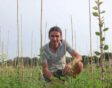 Johan zit gehurkt op het gras bij een fruitboompje.