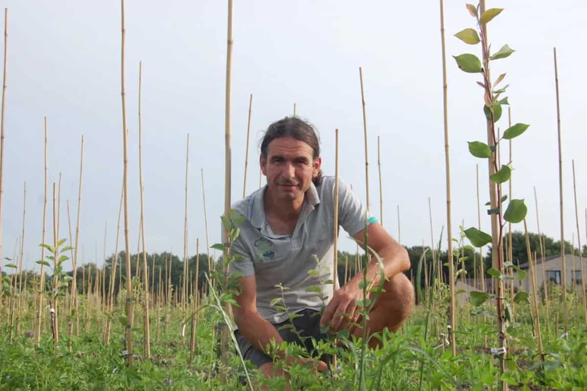 Johan zit gehurkt op het gras bij een fruitboompje.