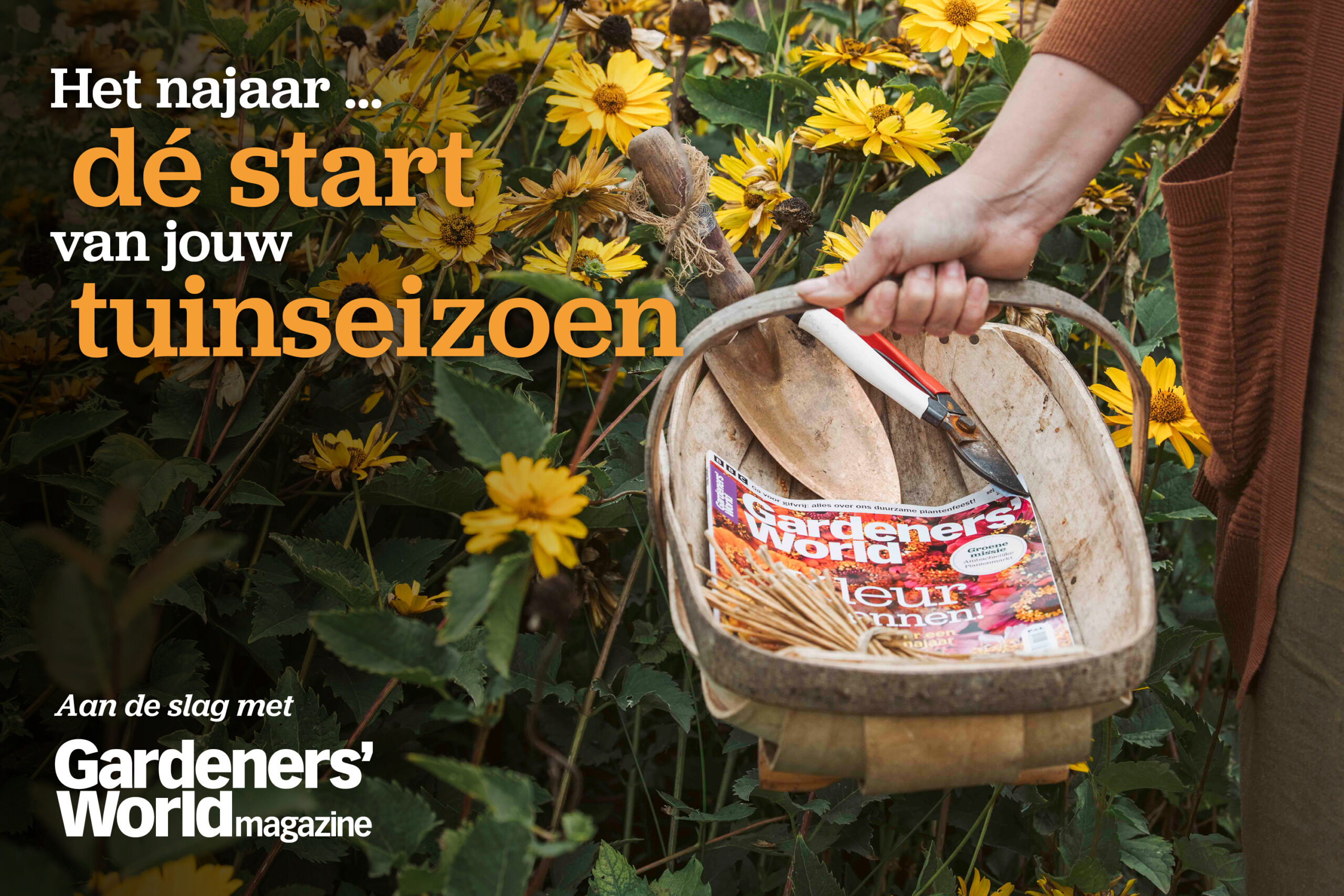 Hand met oogstmand met het een editie van Gardeners' World magazine erin en bloemen op de achtergrond.