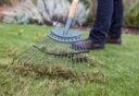 Een hark gaat door het groene gras en neemt dood, bruin materiaal mee.