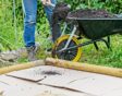 Vrouw schept compost op karton in tuin.