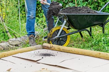 Vrouw schept compost op karton in tuin.
