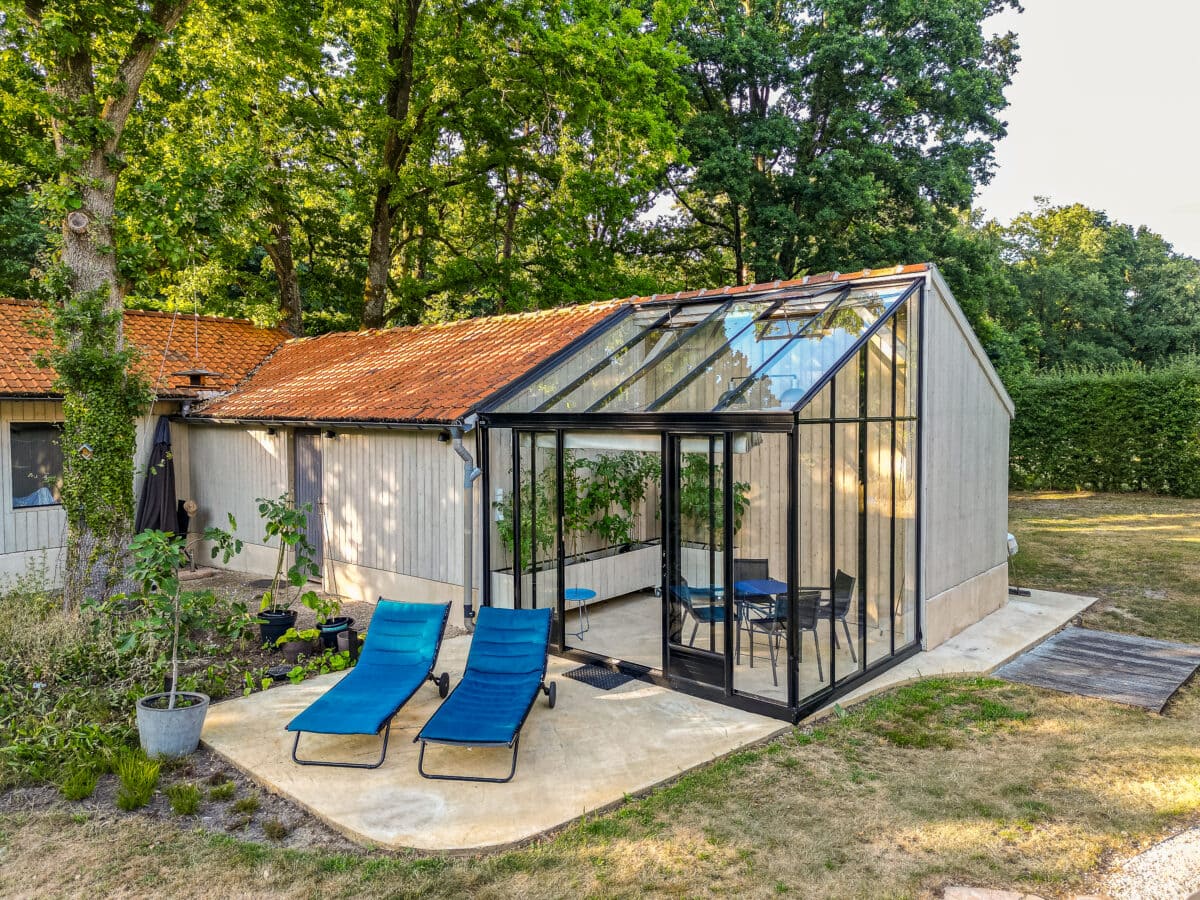 Een serre, aangebouwd aan een verbouwde schuur, met twee ligstoelen ervoor.