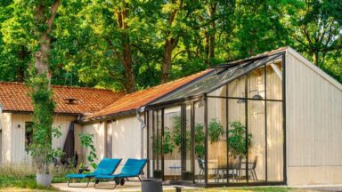 Een serre, aangebouwd aan een verbouwde schuur, met twee ligstoelen en een zwembad ervoor.