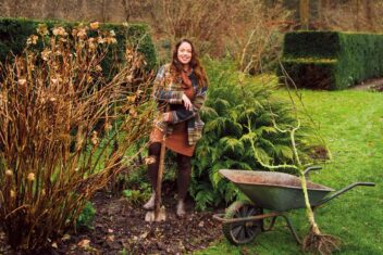 Anne Wieggers met een spade naast een kruiwagen en een kleine boom.