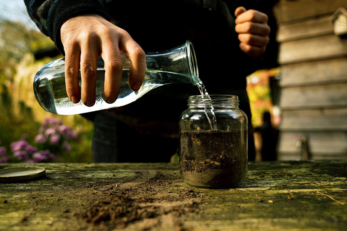 Water wordt in glazen pot met aarde gegoten