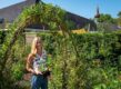 vrouw staat met bloemen in groene tuin voor gebouw.