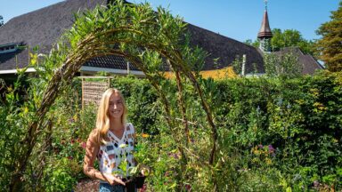 vrouw staat met bloemen in groene tuin voor gebouw.