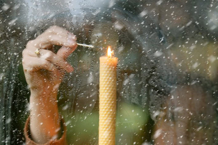 Vrouw steekt een bijenwaskaars aan met lucifer achter het raam.