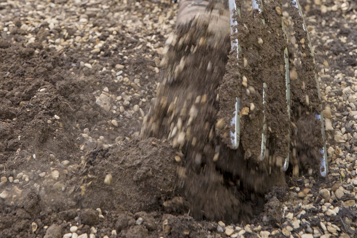 Mix de grond met een tuinvork met het grind