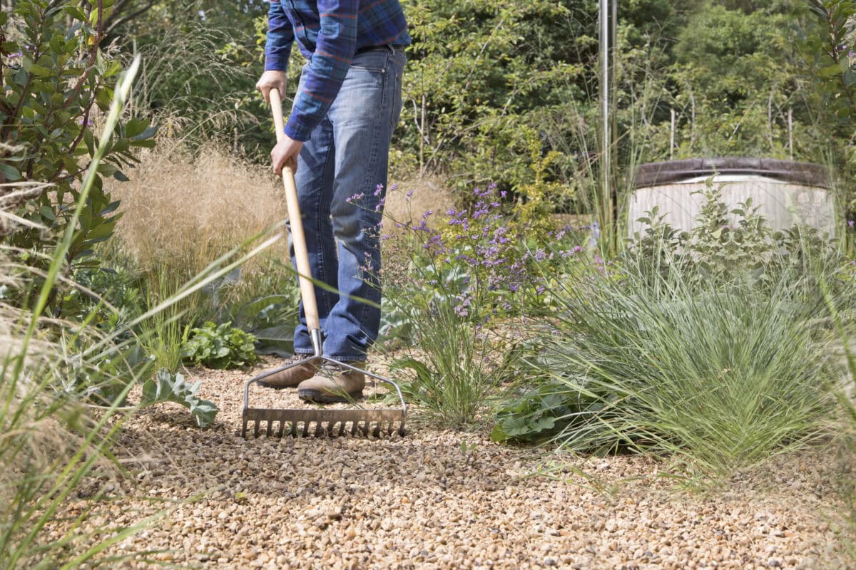 Man gaat met een hark door het grind in de tuin.