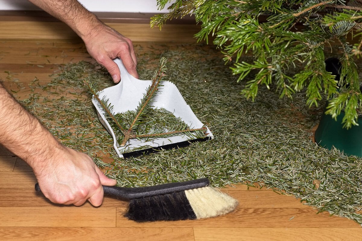 Iemand veegt met stoffer en blik naalden van de kerstboom op de grond.