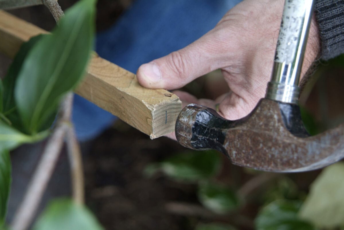 Iemand maakt of repareert een steunconstructie met een houten balk en een hamer.