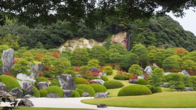 Een pad door een Japanse tuin bij het Adacht Museum of Art, met veel strak gesnoeide planten.