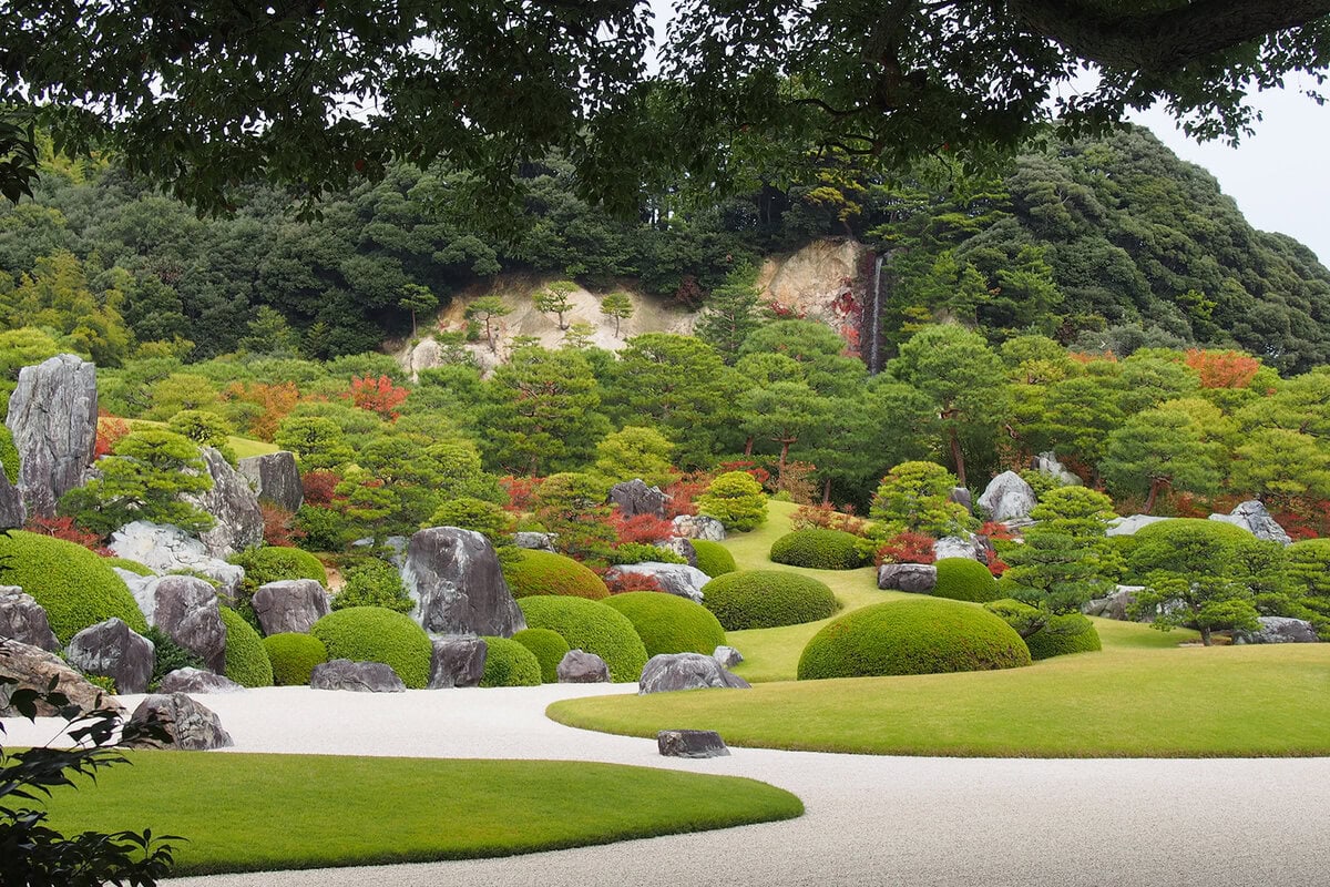 Een pad door een Japanse tuin bij het Adacht Museum of Art, met veel strak gesnoeide planten.