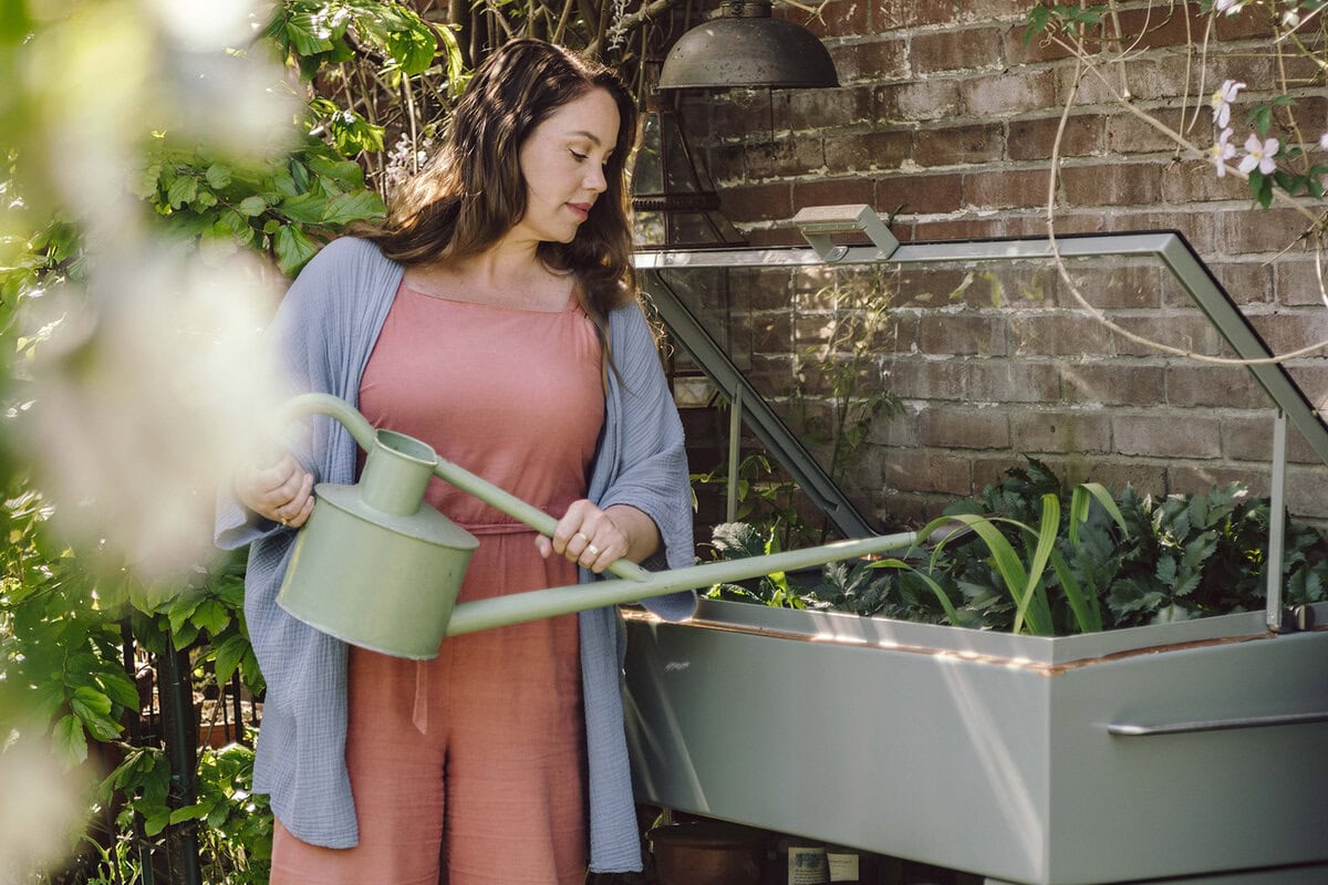 Anne geeft moestuinplanten in een kweekkas water met een gieter