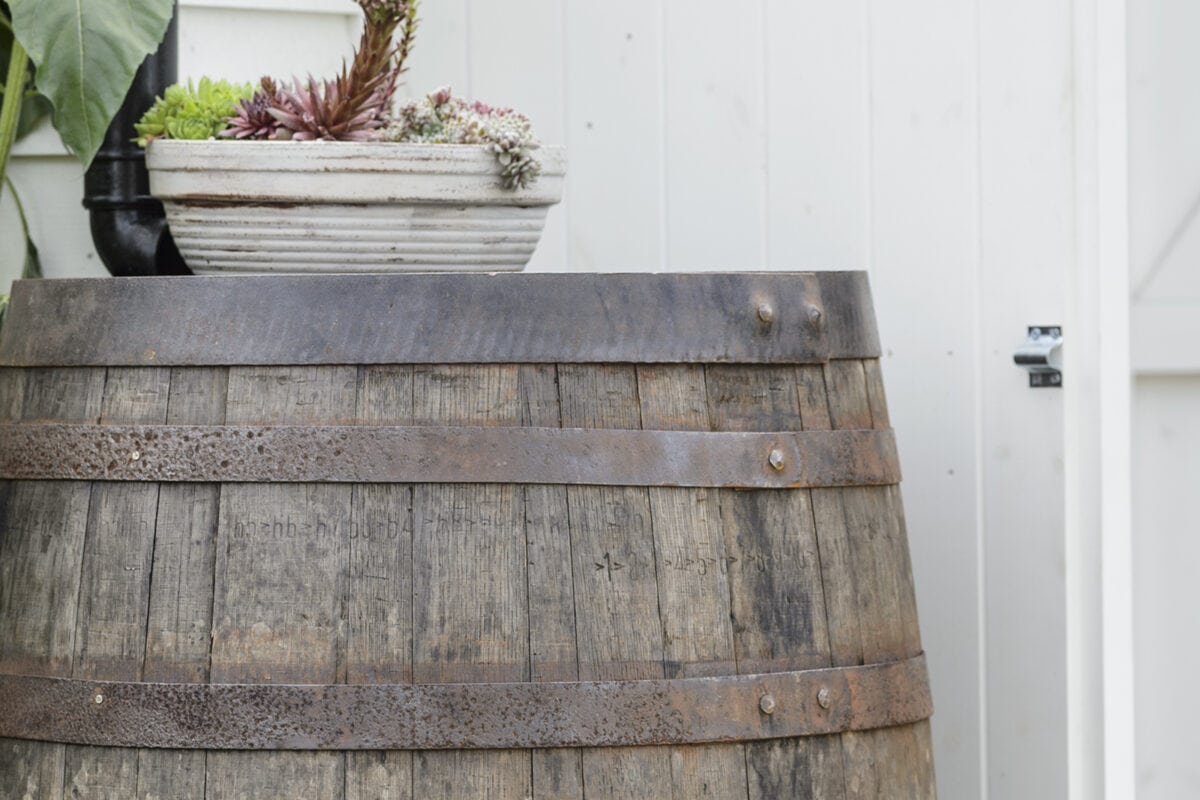 Detail van een houten regenton met daarop een plantenpotje.