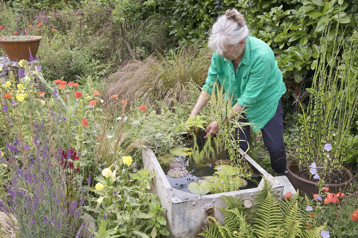 Vrouw maakt tijnvijver in tuin met veel bloemen en dichte beplanting voor tuindieren.