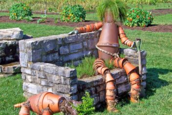 Vogelverschrikker van potten en planten op een stenen bankje naast een hond van potten en planten.