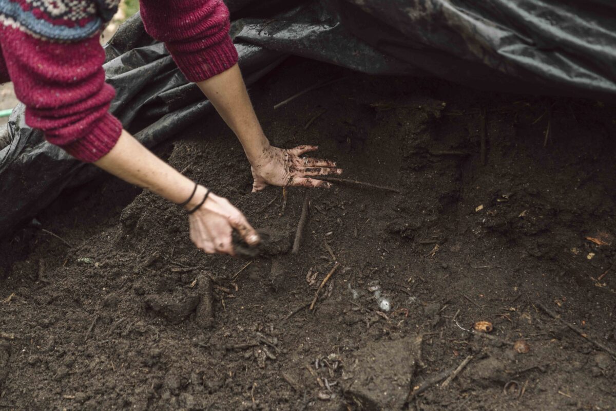 Twee handen laten de compost van de bokashihoop zien.