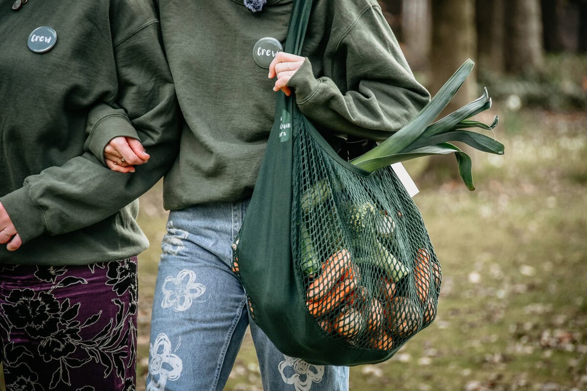 Iemand houdt een tas vol groenten vast.