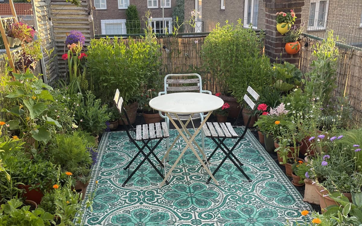 Een sfeervol dakterras vol planten, bloemen, vloerkleed, tafel en stoelen, hekken, doek.