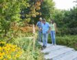 Drie mensen lopen door een tuin met bloeiende planten.