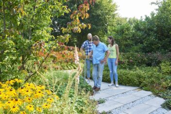 Drie mensen lopen door een tuin met bloeiende planten.