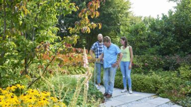 Drie mensen lopen door een tuin met bloeiende planten.