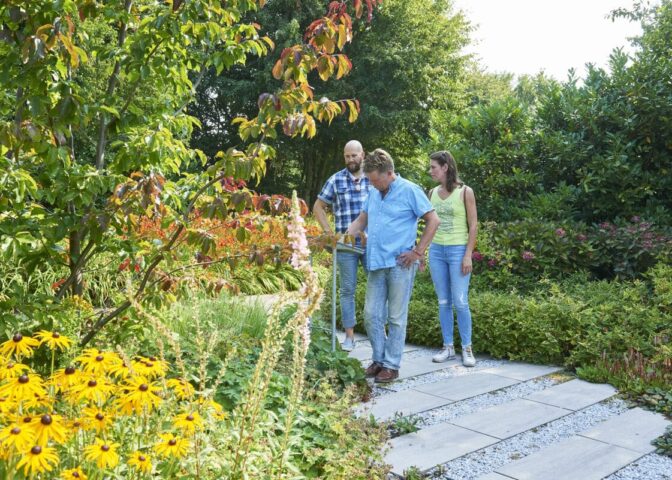 Drie mensen lopen door een tuin met bloeiende planten.