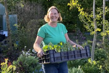 Giny de Jong houdt een tray met planten vast in de tuin.