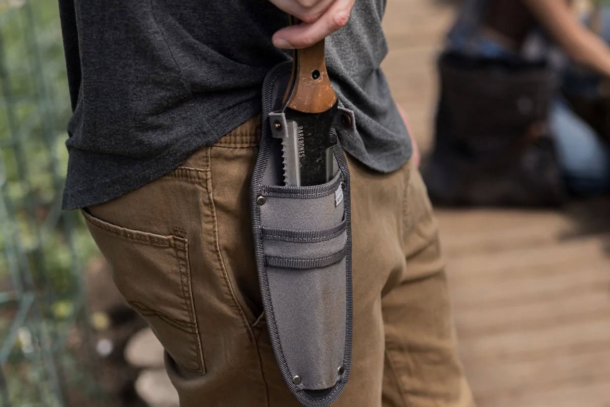 Iemand haalt een hori hori uit een holster om zijn heup.