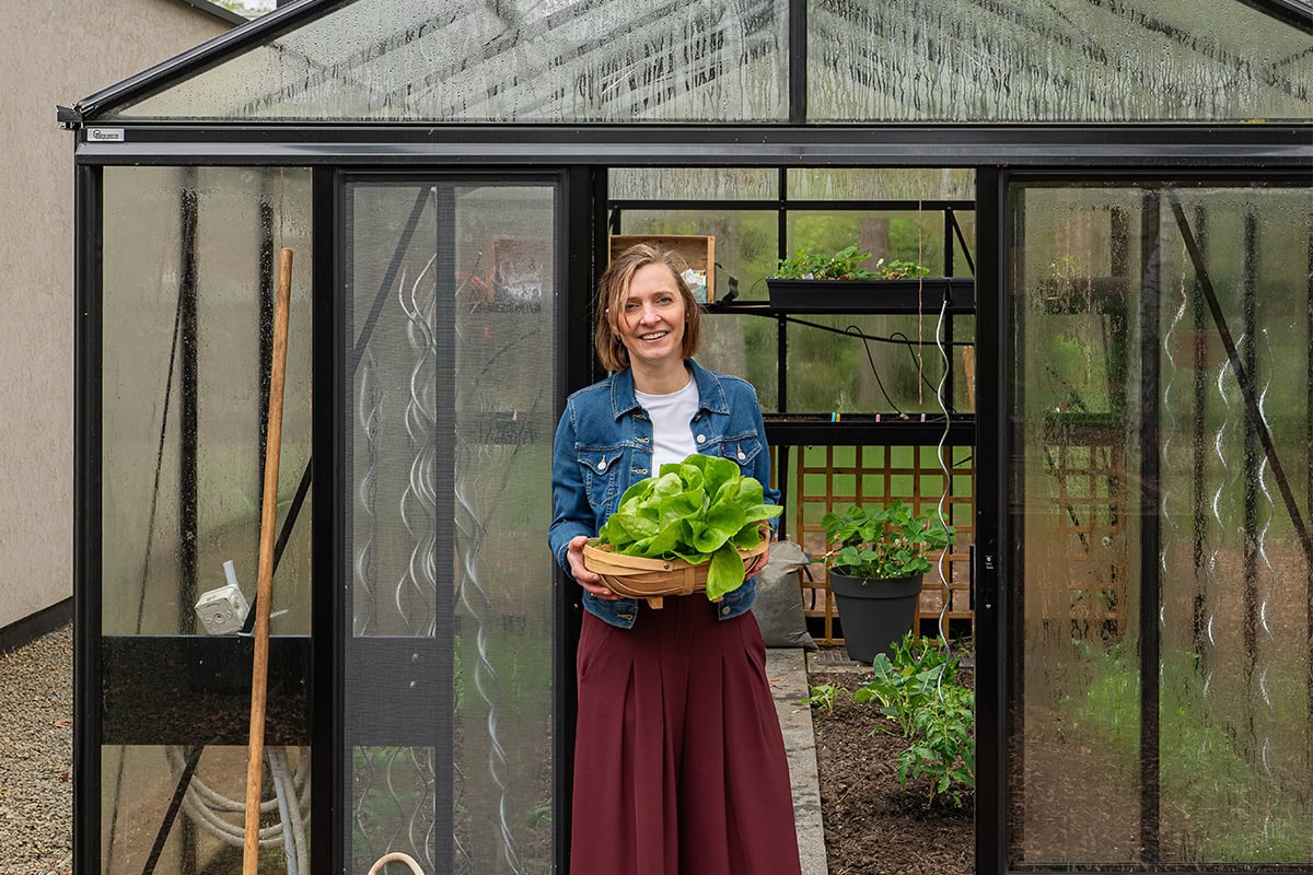 Joke voor de ingang van haar serre met een oogstmand in de handen.