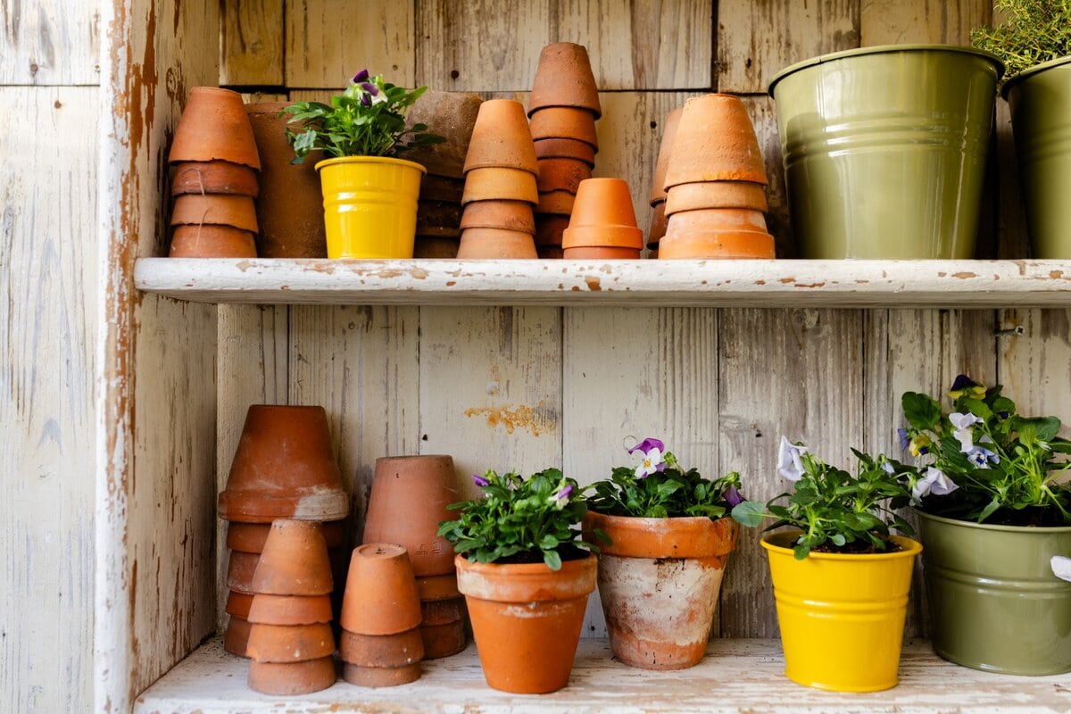Zinken en terracotta potten opgestapeld in een houten kast, met viooltjes in potten erbij.