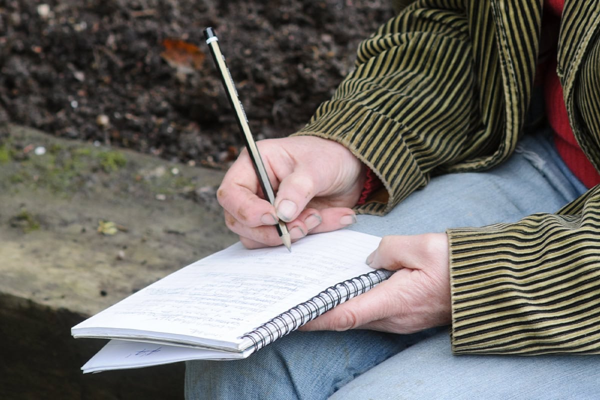 Een hand maakt aantekeningen in een notitieboek, de andere hand houdt het notitieboek vast.