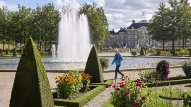 Vrouw wandelt door paleistuinen van Paleis Het Loo, met fontein.