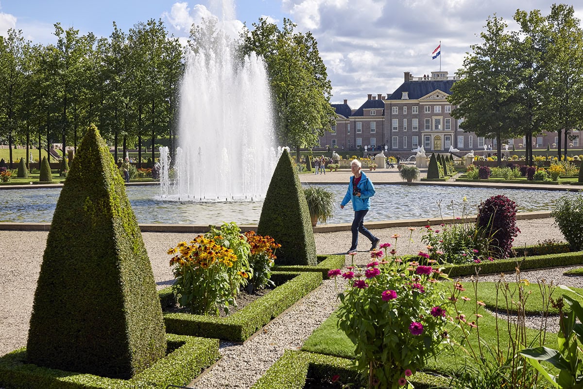 Vrouw wandelt door paleistuinen van Paleis Het Loo, met fontein.