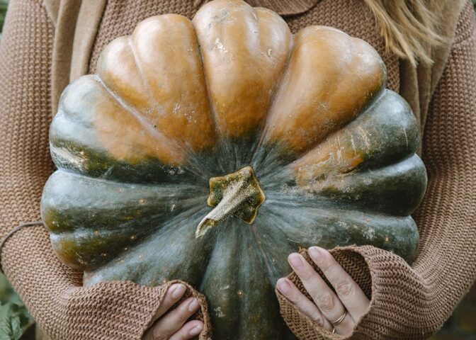 Vrouw draagt een grote pompoen in haar armen.
