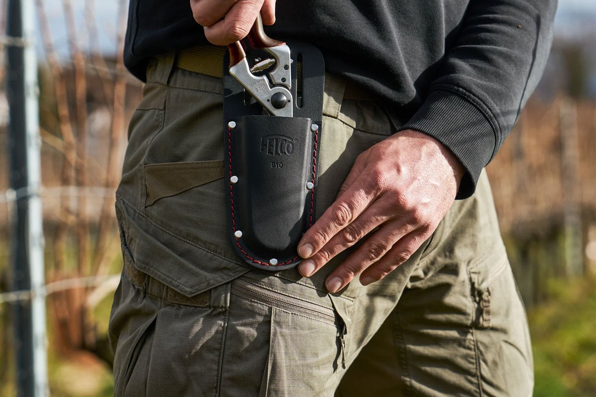 Man stopt snoeischaar in zwarte holster aan zijn broek.