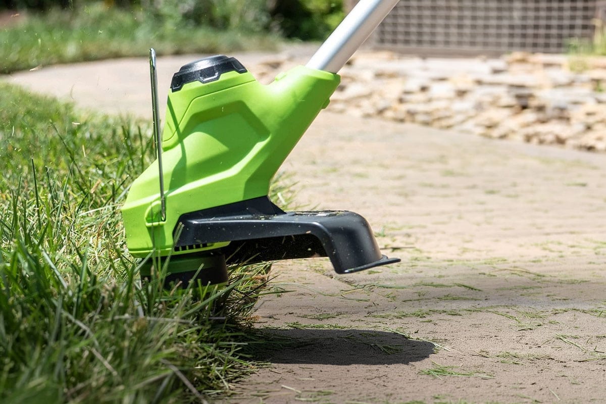 Met een grastrimmer worden de graskanten naast een pad getrimd.