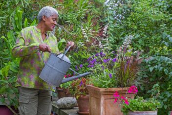 Arit Andersen geeft een pot vol zomerse planten, zoals verbena en pennisetum, water.